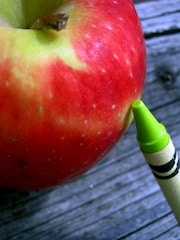 Closeup of an apple with a green crayon leaning on it
