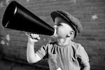 Black and white image of little boy wearing a hat yelling into a small megaphone