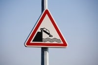 Caution sign with car falling into water