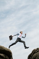 Man holding a briefcase taking a leap across two cliffs