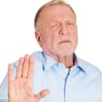 Older man holding up hand with an expression of reluctance