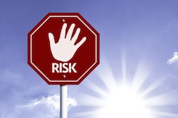 Stop sign with a handprint and "risk" text against sunny skies background
