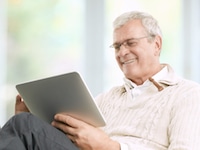 Elderly man sitting down smiling looking at an iPad
