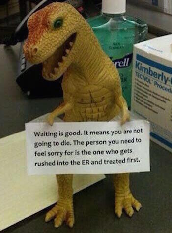 Toy t-rex on desk holding a "waiting is good' sign