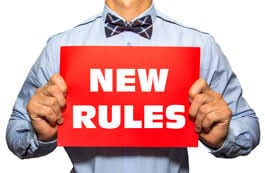 Man wearing bow tie holding up a red "New Rules" sign