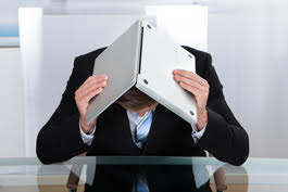 Person wearing suit putting head down in frustration with laptop opened over head