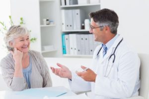 Older female patient sitting in office with male doctor having a discussion, both smiling