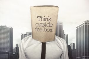 Think outside the box brown paper bag over businessman's head, cityscape background