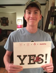 Young man holding up a 'YES!" sign in response to acceptance into college