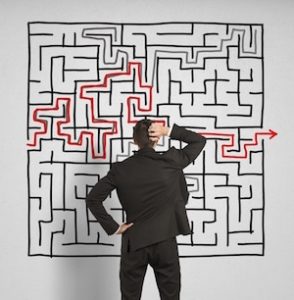 Man in suit looking at large wall maze in confusion