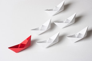 red paper boat leading white paper boats