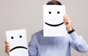 Man holding up a happy face on paper up to his face and a sad face in the other hand