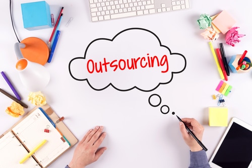 Person drawing a thinking bubble with "Outsourcing" text on a desk