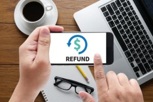 Person sitting at a desk using smartphone with "Refund" arrow & money sign displayed on screen