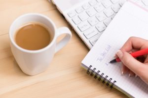 Person sitting at desk, drinking coffee, writing a Healthcare Website Checklist in notebook