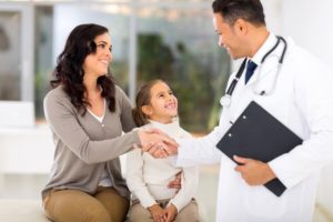 Mother sitting next to young daughter while shaking hands with male doctor