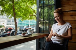 Woman sitting at a cafe window seat looking at smartphone and smiling