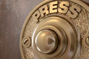 Closeup of a gold doorbell displaying the word "Press" above the button