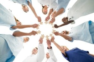 Doctors and nurses standing together in a circle holding puzzle pieces out