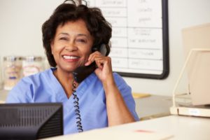 Female nurse sitting at front desk smiling while talking on the phone