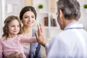 mom holding little girl on lap, daughter high-fiving male doctor