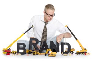 man playing with building vehicle toys and letters spelling out "Brand"
