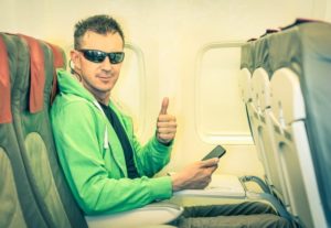 Man wearing sunglasses, sitting on airplane giving a thumbs up