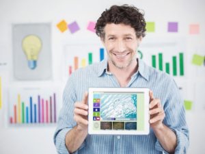 Man holding iPad displaying video while standing in front of large graph ideas on wall