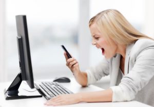Woman screaming into cell phone while sitting at a desk in front of a computer