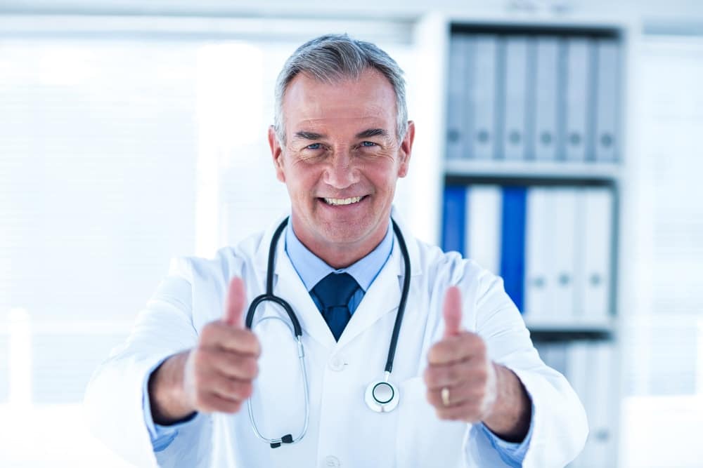 Older male doctor giving two thumbs up, smiling