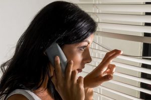 Woman peeking through the blinds  while talking on a telephone