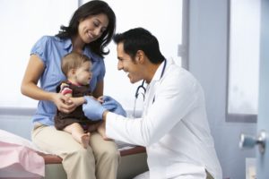 Male doctor playing with baby patient sitting on mom's lap