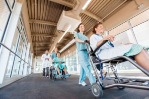 two nurses pushing patients in wheelchairs in hospital hallway
