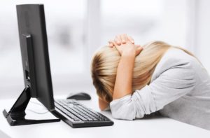 Person holding their head down on desk in frustration in front of a computer