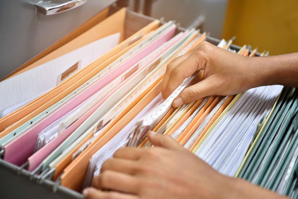 Person's hands rummaging through file cabinet files