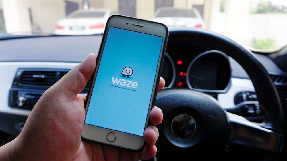 person in car holding a cellphone with the waze advertising app displayed on screen
