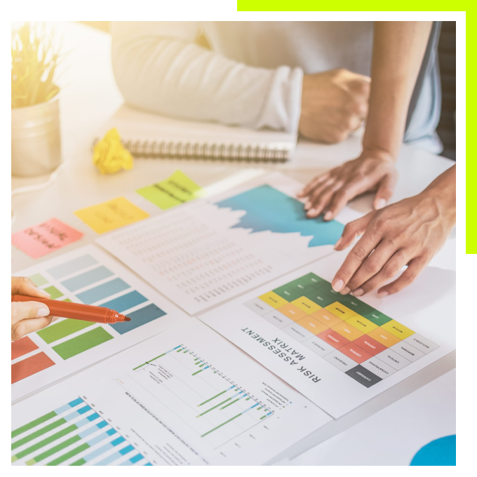 A top-down view of people collaborating over business charts, graphs, and a risk assessment matrix on a desk.